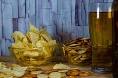 Soğuk bira ve dalgalı patates cipsi kasede ve ahşap masada tuzlu çerezler.