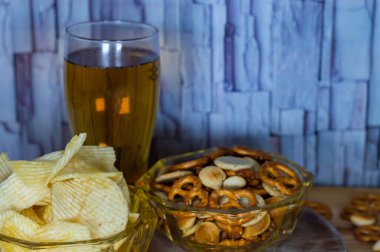 Soğuk bira ve dalgalı patates cipsi kasede ve ahşap masada tuzlu çerezler.