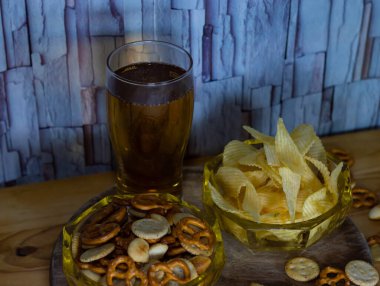 Soğuk bira ve dalgalı patates cipsi kasede ve ahşap masada tuzlu çerezler.
