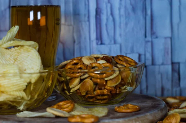 Cold beer and wavy potato chips in a bowl and salty snacks pretzel on a wood table