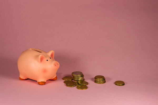 Close-Up Of pink Piggy Bank With Coins Against Pink Background - Concept of saving money - Copy space area