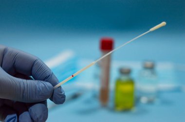 Mavi arka planda aşılar ve tıbbi maske olan bulanık arkaplanlı Coronavirus testi için pamuklu çubukla doktorun eli, boş kopya alanı...