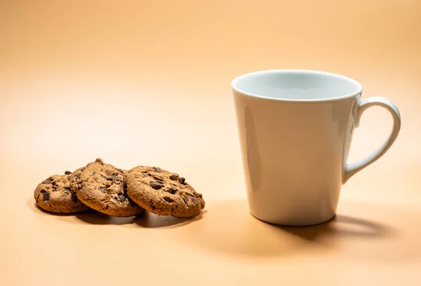 Beyaz bardak sütü ve boş arka planda üç siyah çikolatalı kurabiyeyi kapat. Boşluğu kopyala. Sarı altın arkaplan