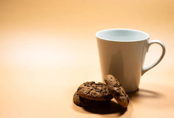 Beyaz bardak sütü ve boş arka planda koyu çikolata parçacıklı kurabiyeleri kapatın. Boşluğu kopyalayın. Sarı altın arkaplan