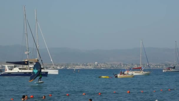 Человек практикует спорт крыла фольги в море между лодками в летний день — стоковое видео