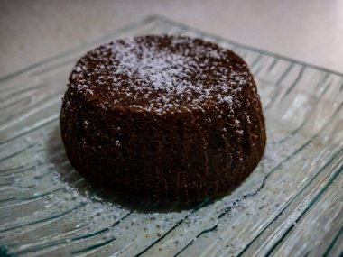Bardak tabakta servis edilen pudra şekerli küçük çikolatalı pasta.