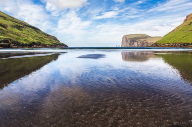 Faroe Adaları 'ndaki Tjornuvik' in Black SBlack kumsalındaki yansımalar, parlak mavi gökyüzü altında yeşil kayalıklar ve deniz yığınlarının yansımaları Risin ve Kellingin ve Tjornuvik, Faroe sahilleri.