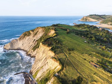 İspanya 'nın kuzeyinde, Bask Bölgesi' ndeki yeşil tarım arazileri ve tepelerle çevrili Atlantik Okyanusu 'yla buluşan engebeli sahil uçurumlarının insansız hava aracı görüntüsü altın akşam ışığı sırasında.