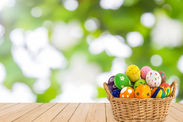 Ahşap doku üzerinde yeşil bokeh sepetteki renkli Paskalya yumurtaları 