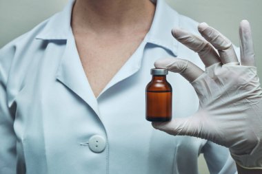 İlaç ampulünü gösteren eldivenler giymiş bir hemşirenin elleri görülüyor..