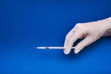 Mavi arkaplanda fotokopi alanı enjekte etmeye hazır tıbbi bir el görüntüsü.