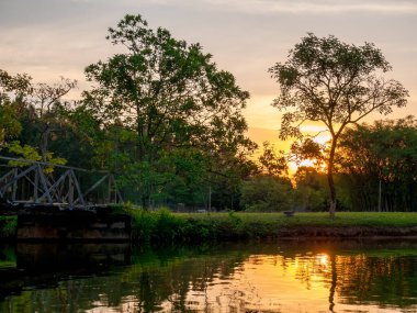 Gün batımı manzarası gölde yansıyan ağaçlar ve gökyüzü.