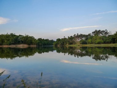 Gün batımı manzarası gölde yansıyan ağaçlar ve gökyüzü.