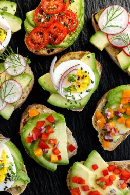 Siyah bir taş zemin üzerine çeşitli soslar ile avokado kanepeler