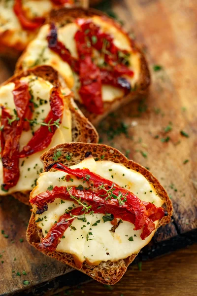 Toasts with smoked sheep milk cheese, sun-dried tomatoes and herbs — Stock Photo, Image