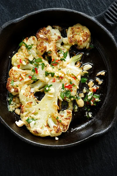 Roasted cauliflower slice with the addition of aromatic sauce with peanuts, chili and parsley  on a cast-iron frying pan — Stock Photo, Image