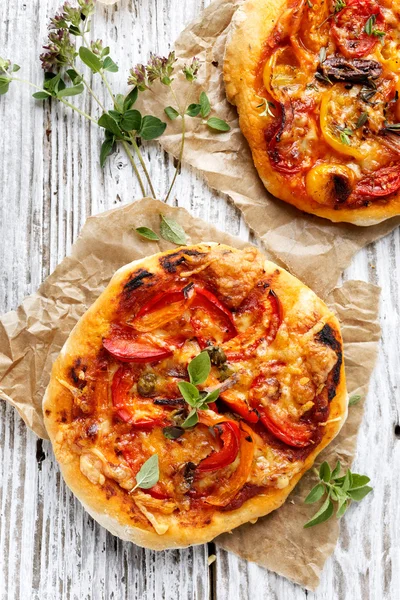 Petite pizza de légumes maison avec ajout de poivre grillé, tomates, fromage et herbes sur une table en bois blanc — Photo