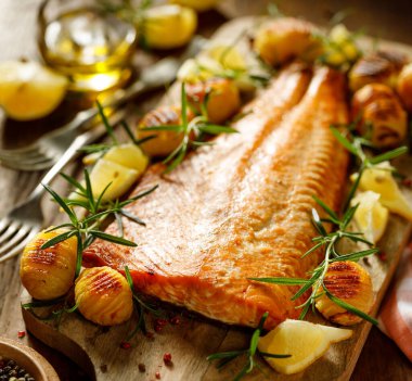 Fırında somon fileto, hasselback patatesli, limonlu ve biberiyeli ahşap tahtada servis edilen yakın görüş.