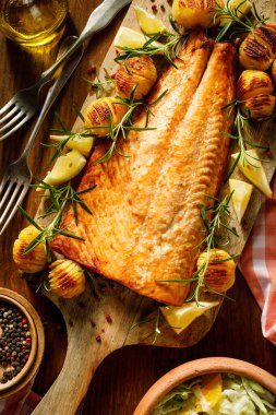 Fırında somon fileto, hasselback patatesli, limonlu ve biberiyeli ahşap tahtada servis edilmiş.