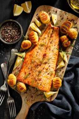 Fırında somon fileto, hasselback patatesli, limonlu ve biberiyeli ahşap tahtada servis edilmiş.