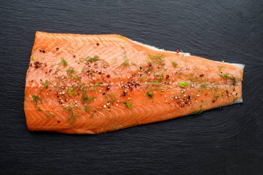 Baharatlı taze somon filetosu ve siyah arka planda taze otlar. 
