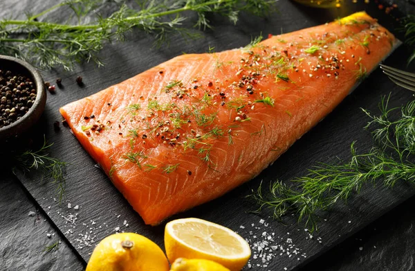 Fresh salmon fillet with spices and fresh herbs on a black background close up view