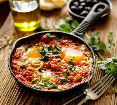 Geleneksel Shakshuka tabağı ahşap masada dökme demir bir tavada servis edilir.