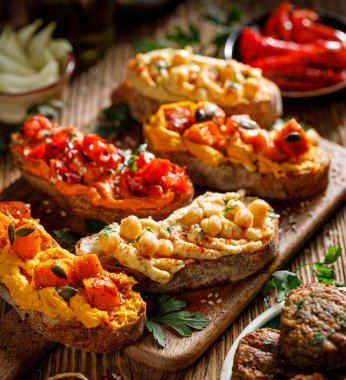 Humus sandviçleri, farklı türde humuslarla ahşap bir tahtanın üzerinde servis edilir, yakın görüş. Sağlıklı ve lezzetli parti yemekleri.