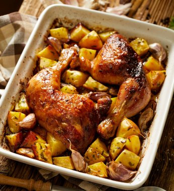 Pişmiş tavuk budu ve patatesler ahşap bir masada yakın plan çekimde. 