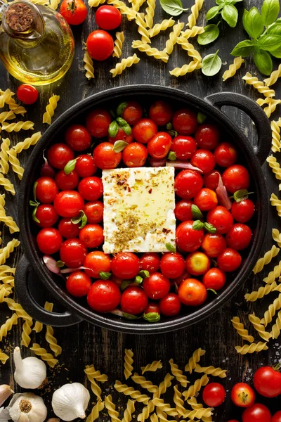 Feta pasta, ingredients for making pasta sauce based on feta cheese and cherry tomatoes, top view. A popular dish.