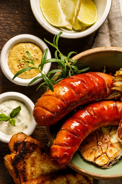 Grilled sausages, garlic and onions with different kinds of dips — Stock Photo, Image