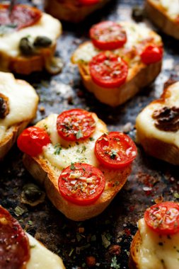 Crostini ile peynir, domates ve karanlık bir arka plan üzerinde otlar