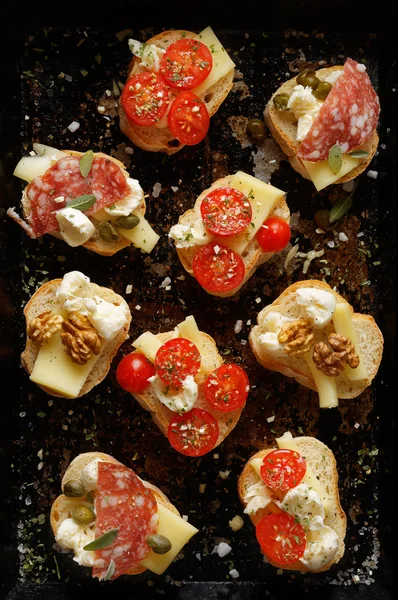 Small canapes with different toppings on a dark background — Stock Photo, Image