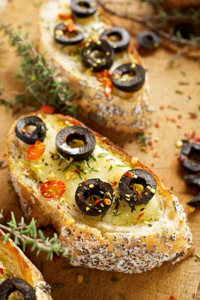 Toasted baguette with cheese, blck olives,chili pepper and thyme — Stock Photo, Image