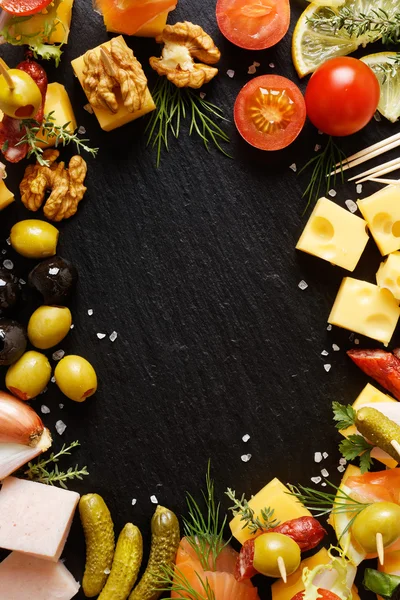 Aantal verschillende smakelijke hapjes, snacks en ingrediënten op een zwarte achtergrond — Stockfoto