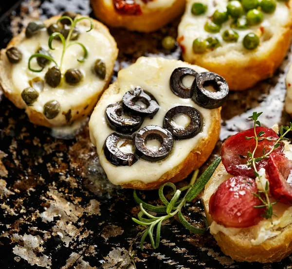 Crostini com coberturas diferentes sobre fundo escuro. Aperitivos deliciosos — Fotografia de Stock