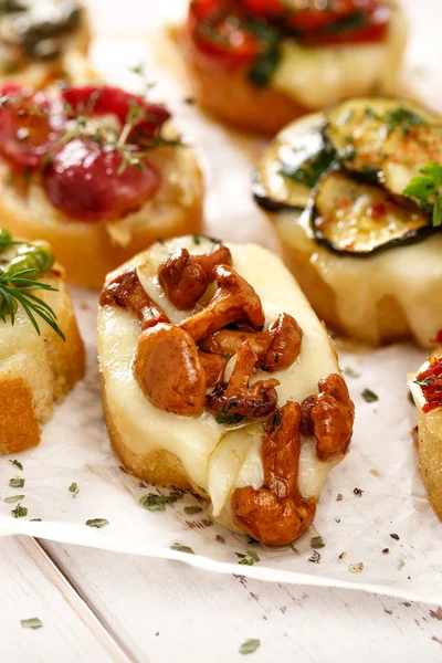 Crostini with addition of chanterelle mushroom and melted cheese on white table closeup — Stock Photo, Image