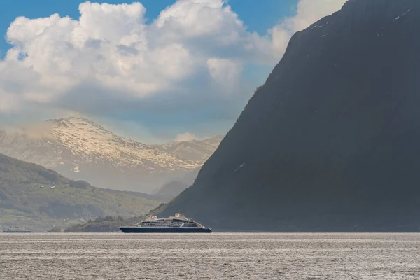 Hareid, Norway - 2020 Mayıs 25. Norveç fiyordunun içinde, arka planda karla kaplı dağlar olan bir gemi..