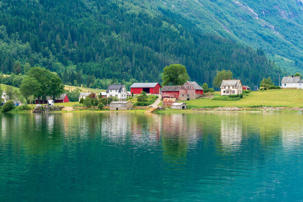 ЛОЭН, НОРВЕГИЯ - 20 июня. Зеленая вода Олден с норвежскими фермами позади.
