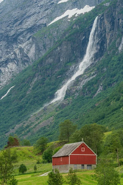 LOEN, NORway - 2020 HAZİRAN 20 Dağın ve şelalenin altındaki kırmızı çiftlik evi..