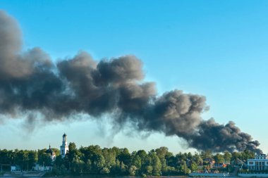 Yanan bir apartmandan mavi gökyüzüne doğru yükselen tehlikeli siyah duman bulutları