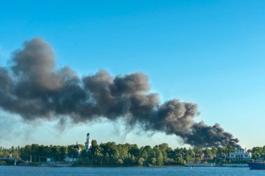 Yanan bir apartmandan mavi gökyüzüne doğru yükselen tehlikeli siyah duman bulutları
