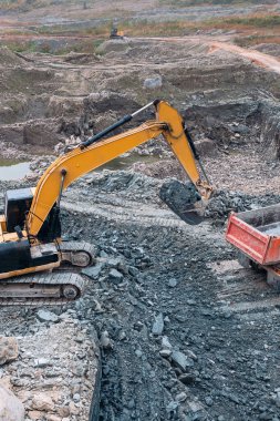 Toprağı kazıcı kovayla kamyona yükleme işlemi toprak bir yolun arka planına karşı.