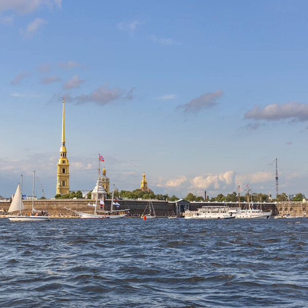 Small sailboats and a white tourist ship are moored on the Neva at the walls of the Peter and Paul Fortress