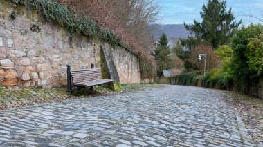 Küçük Alman kasabası Marburg 'da dik bir kaldırım kenarındaki ahşap koltuklu modern bank.