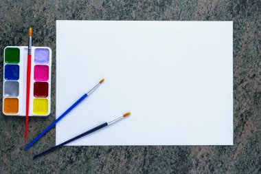 Beyaz kağıt, suluboya bir set ve koyu mermer bir yüzey üzerinde çeşitli fırçalar