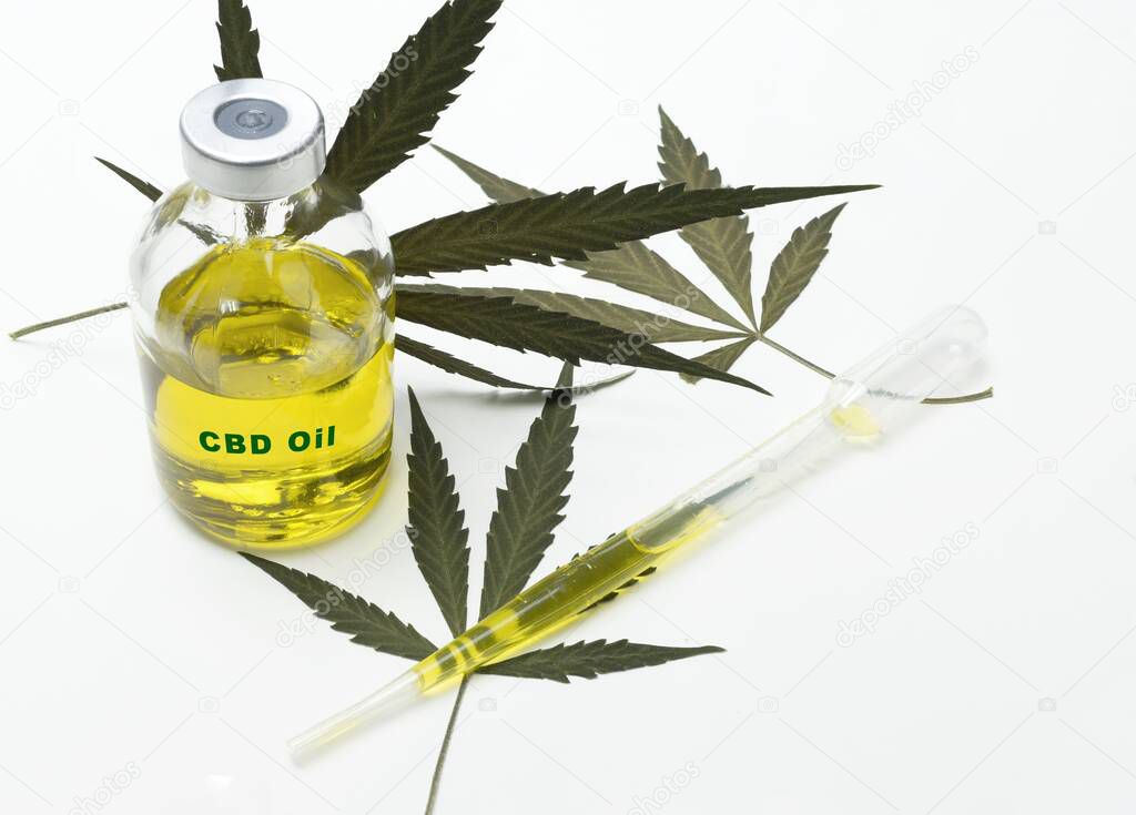 A bottle with medical marijuana oil with the inscription cbs oil on a white background with some dried marijuana leaves