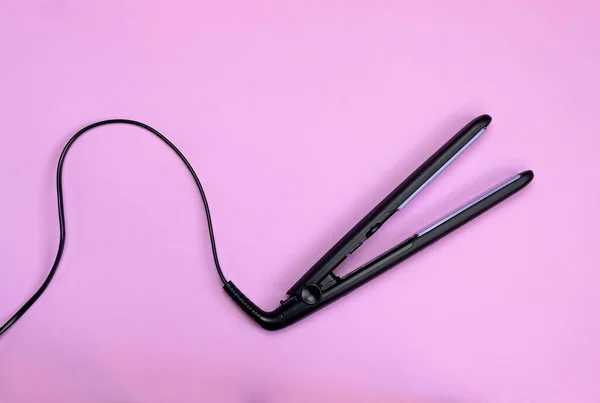 Siyah kablolu saç düzleştirici pembe arka planda izole edilmiş.