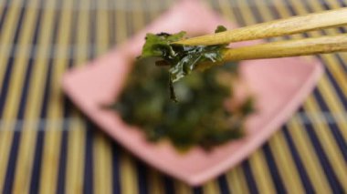 Kameraya su verilmiş Japon wakame deniz yosunu ve Asya yemek çubukları gösteriliyor.