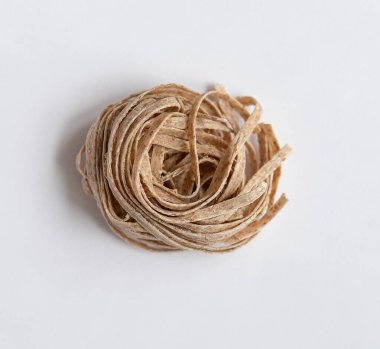 Beyaz arka planda bir porsiyon çiğ, kahverengi makarna. Gıda proteini, karbonhidrat ve lif açısından zengin graham unundan yapılmış leziz bir makarna.